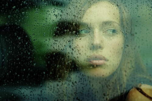 Donna-che-guarda-attraverso-un-vetro-con-gocce-di-pioggia