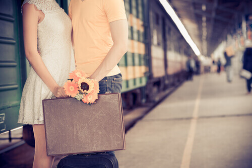 coppia alla stazione dei treni, valigia e mazzo di fiori