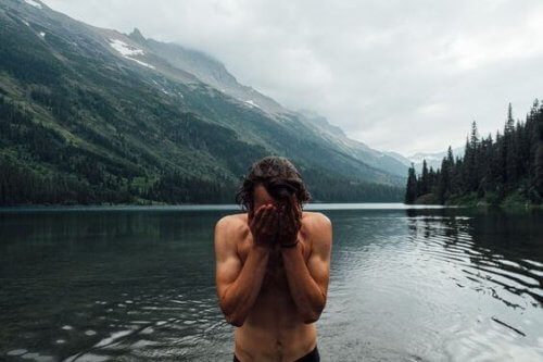 uomo con mani sul viso in un lago con montagne