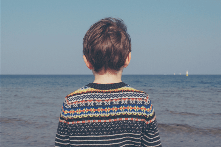 Bambino di spalle davanti al mare.