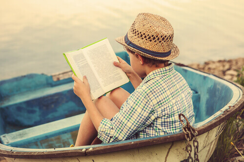 Bambino che legge un libro in una barca sulla spiaggia