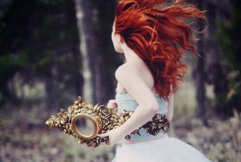 Donna con i capelli rossi corre tenendo uno specchio