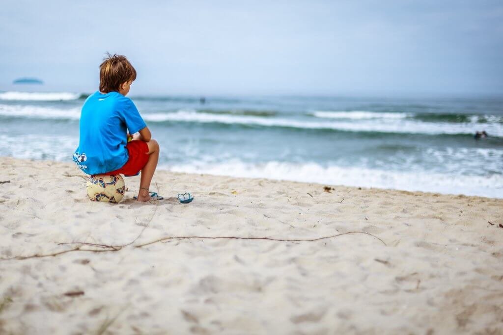 Bambino in spiaggia seduto su una palla mentre guarda verso il mare
