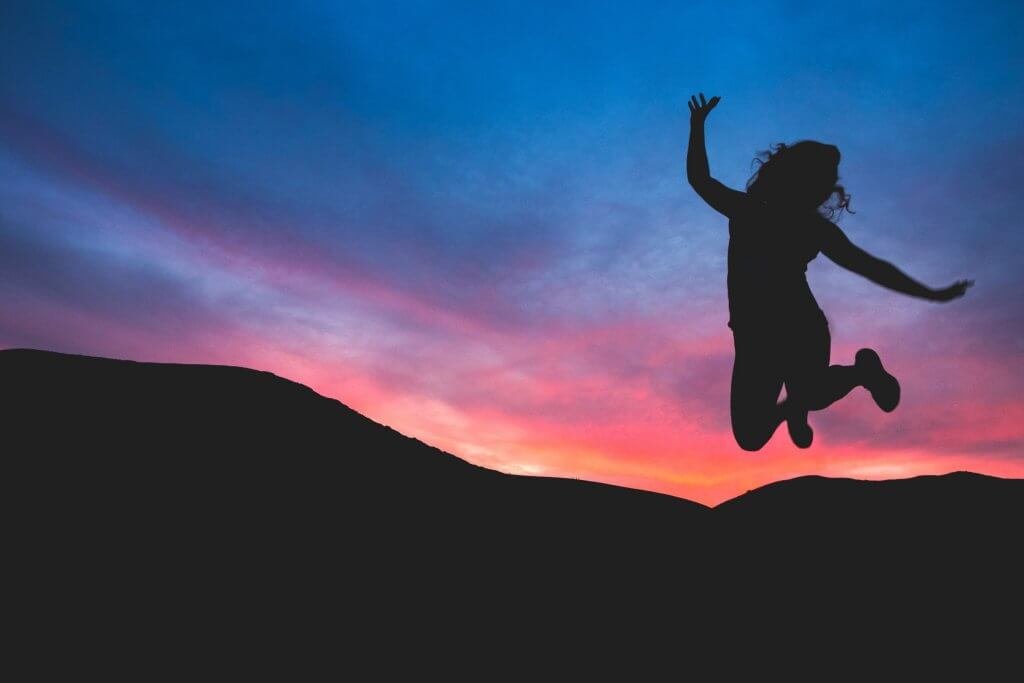 Donna che salta felice davanti ad un tramonto