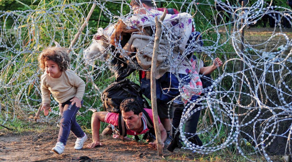 Famiglia di rifugiati che passa sotto il filo spinato
