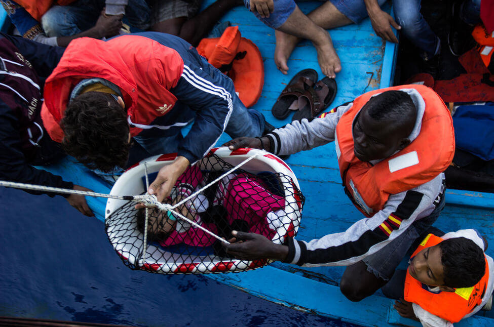 Immigrati che calano un neonato su un barcone