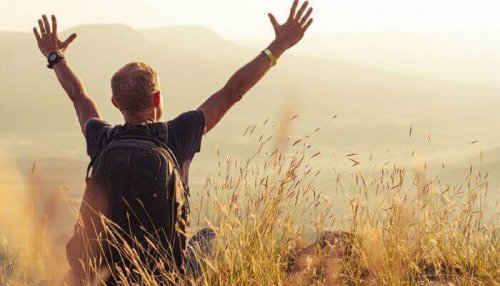 Uomo in campo con zaino in spalla e braccia in alto
