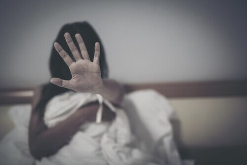 Donna a letto spaventata con mano davanti