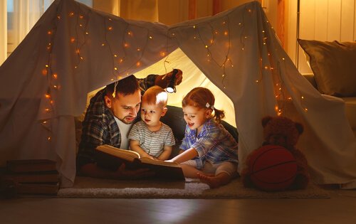 Papà che legge con i suoi bambini dentro a una tenda