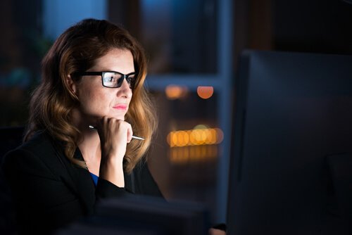 Donna con occhiali e penna che guarda computer di notte