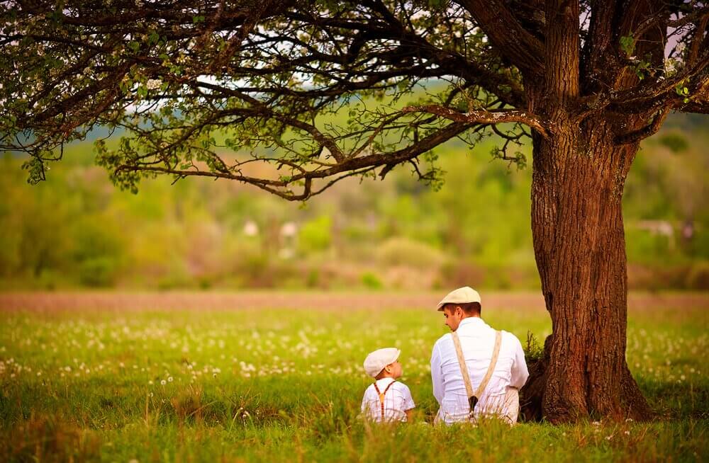 Padre e figlio seduti sotto ad albero