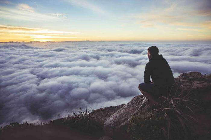 Uomo chinato su montagna che guarda nuvole