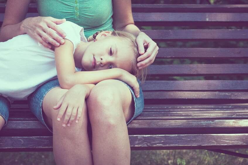 Bambina triste con testa appoggiata su gambe della madre