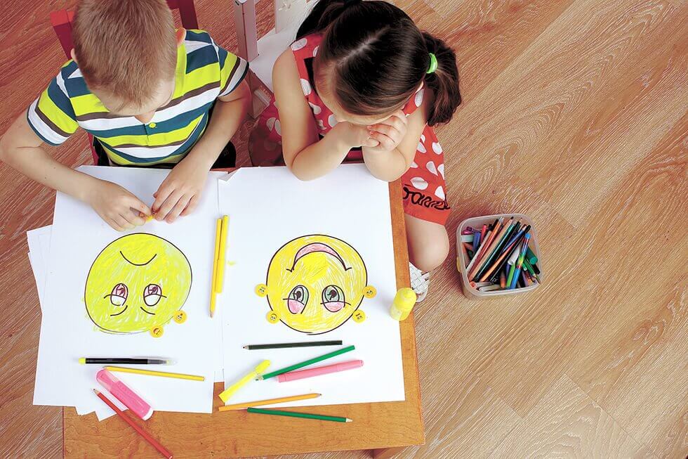 Bambini che disegnano faccine sorridenti e tristi