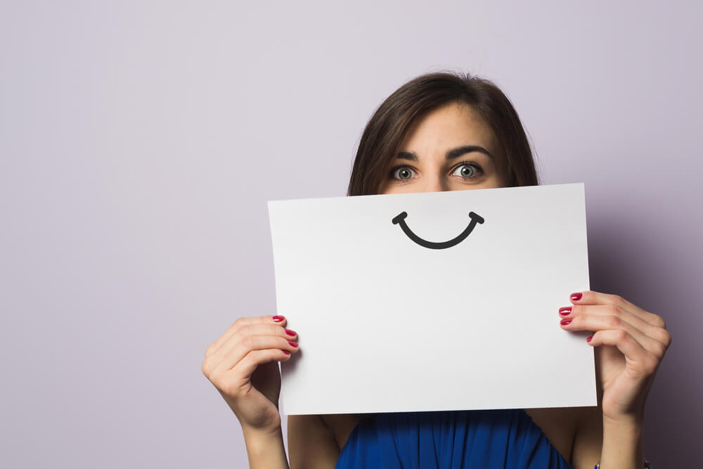 Donna positiva con foglio con disegnato sorriso davanti al volto