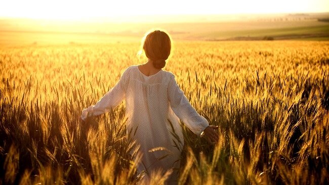 Donna vestita di bianco che cammina in campo di grano