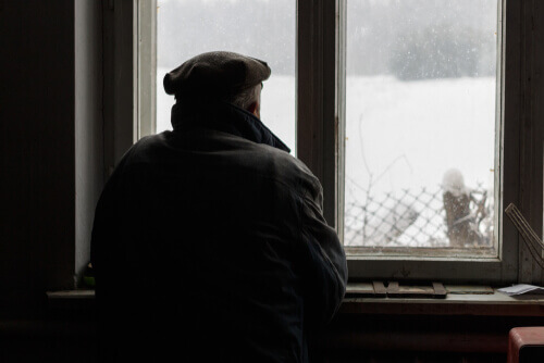 Anziano che guarda la neve dalla finestra