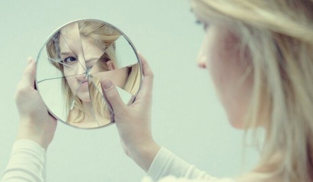 Donna che si guarda in specchio rotto