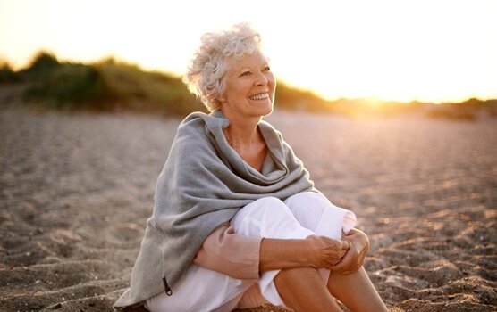 Donna anziana da sola e sorridente seduta su spiaggia
