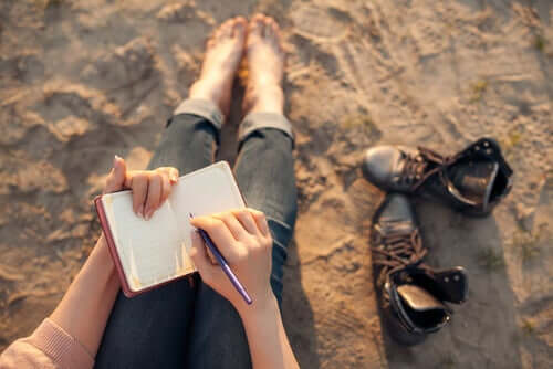 Donna che scrive su un taccuino seduta sulla sabbia