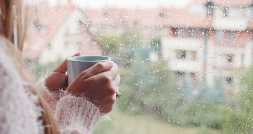 Donna con una tazza di caffè in mano che guarda dalla finestra