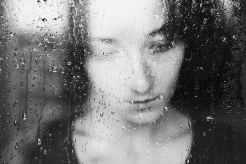 Sentirsi tristi nelle giornate grigie donna che piange davanti alla finestra bagnata.