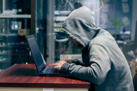 Uomo con cappuccio al computer che sfrutta la psicologia del phishing.