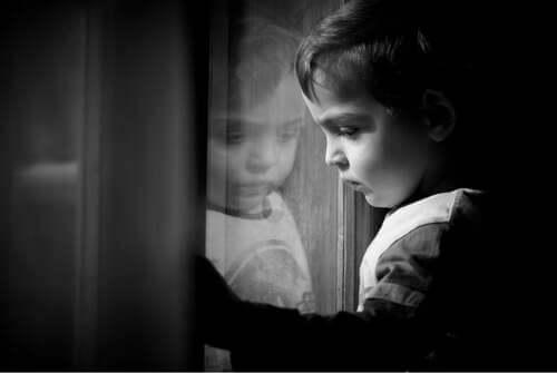Bambino triste che guarda fuori dalla finestra.