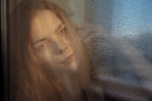 Donna che guarda la pioggia attraverso una finestra.
