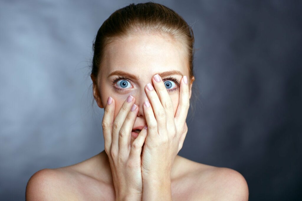 Donna terrorizzata con mani sul viso.