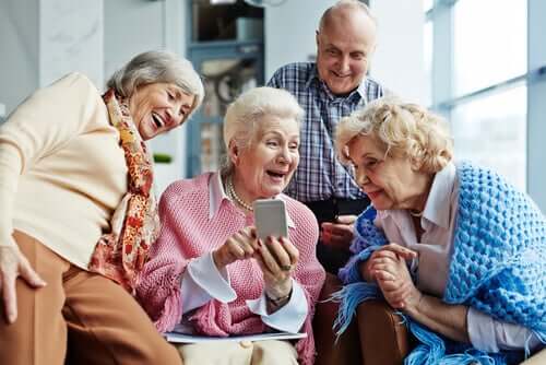 Persone anziane che ridono e si divertono guardando delle foto sul telefono.