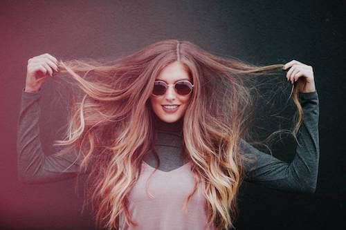 Giovane donna con occhiali che si tocca i lunghi capelli.