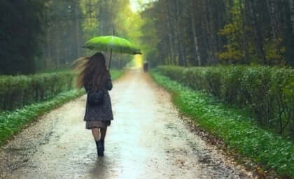 Ragazza cammina sotto la pioggia con un ombrello verde.