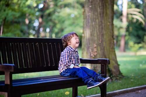 Bambino che piange seduto su una panchina in un parco.