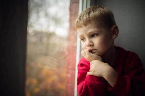 Bambino pensieroso che guarda dalla finestra.
