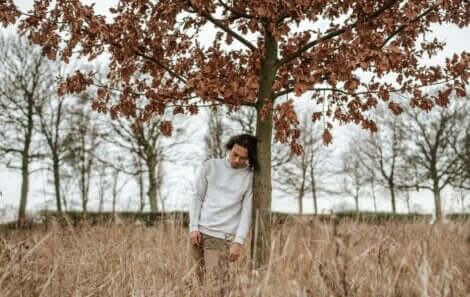 Ragazzo appoggiato al tronco di un albero.