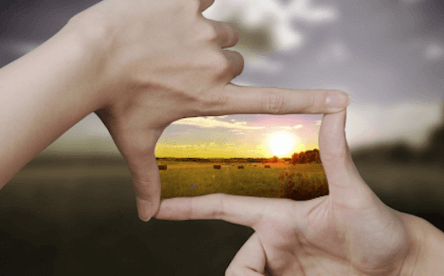 Mani posizionate a forma di inquadratura che inquadrano il sole al tramonto.