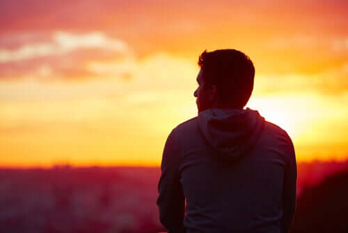 Ragazzo di spalle che guarda il tramonto non sa se accettare e rassegnare.