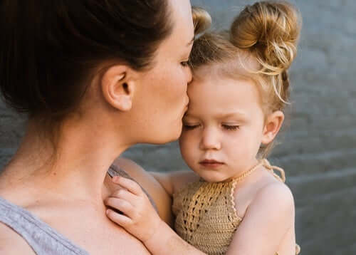 Mamma che bacia la figlia in fronte.
