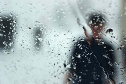 Silhouette di uomo dietro una finestra bagnata dalla pioggia.