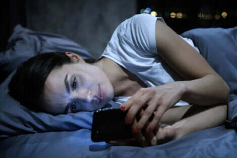 Innamorarsi a distanza e donna a letto guarda il cellulare.