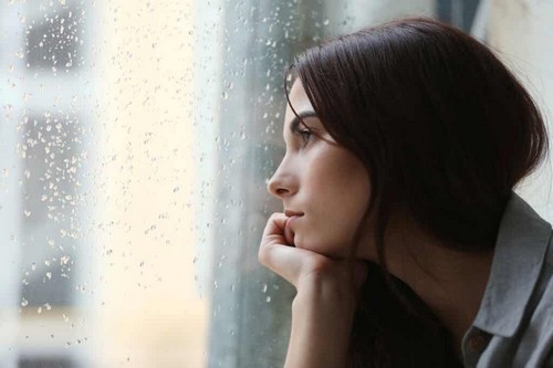 Una donna triste che guarda dalla finestra.