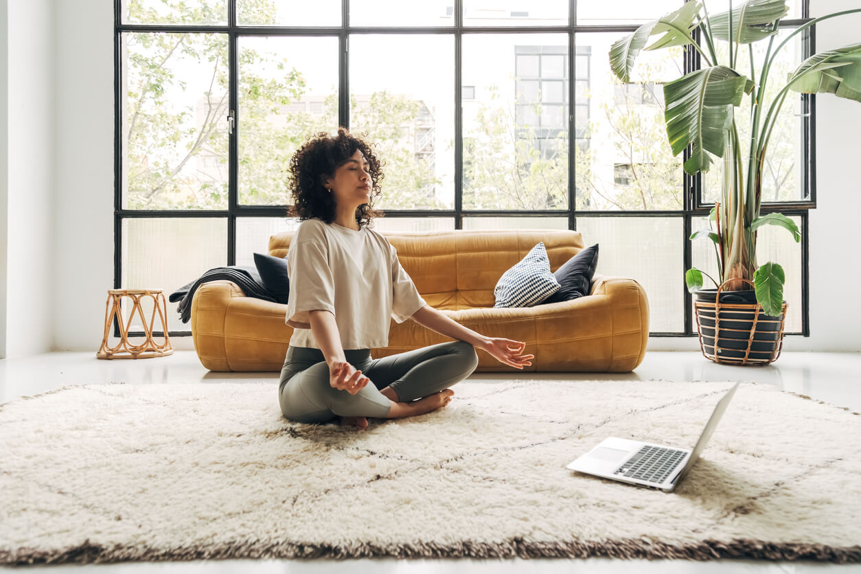 Giovane donna latina multirazziale che medita a casa con una lezione di meditazione video online utilizzando un computer portatile. Concetto di meditazione e spiritualità.